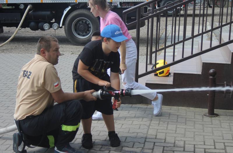 Na zdjęciu chłopiec trzymającego węża przeciwpożarowego