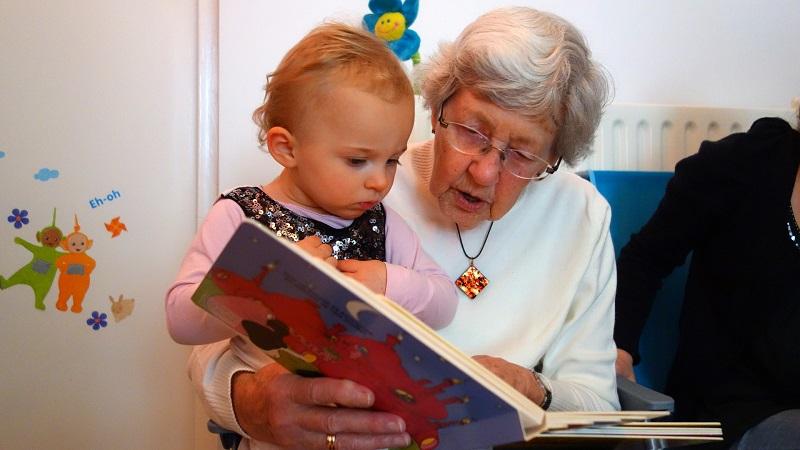 na zdjęciu dziecko czytające książkę z babcią