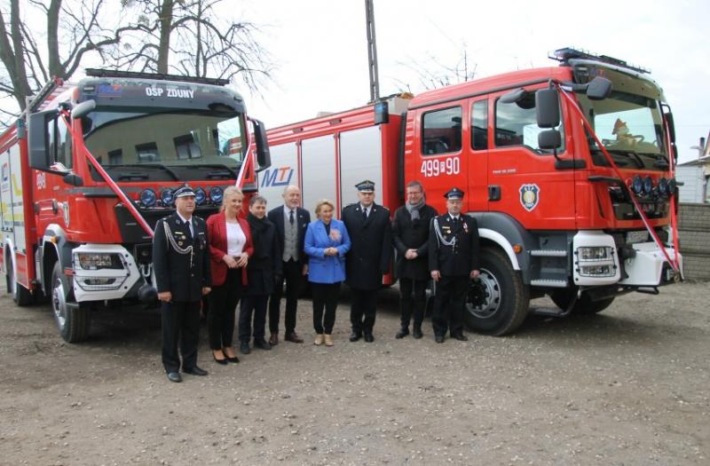 Na zdjęciu Szef Gabinetu Politycznego Minister Marleny Maląg, europoseł i posłowie,  burmistrz Zduz oraz OSP Zduny przy przekazanych samochodach ratowniczo-gaśniczych